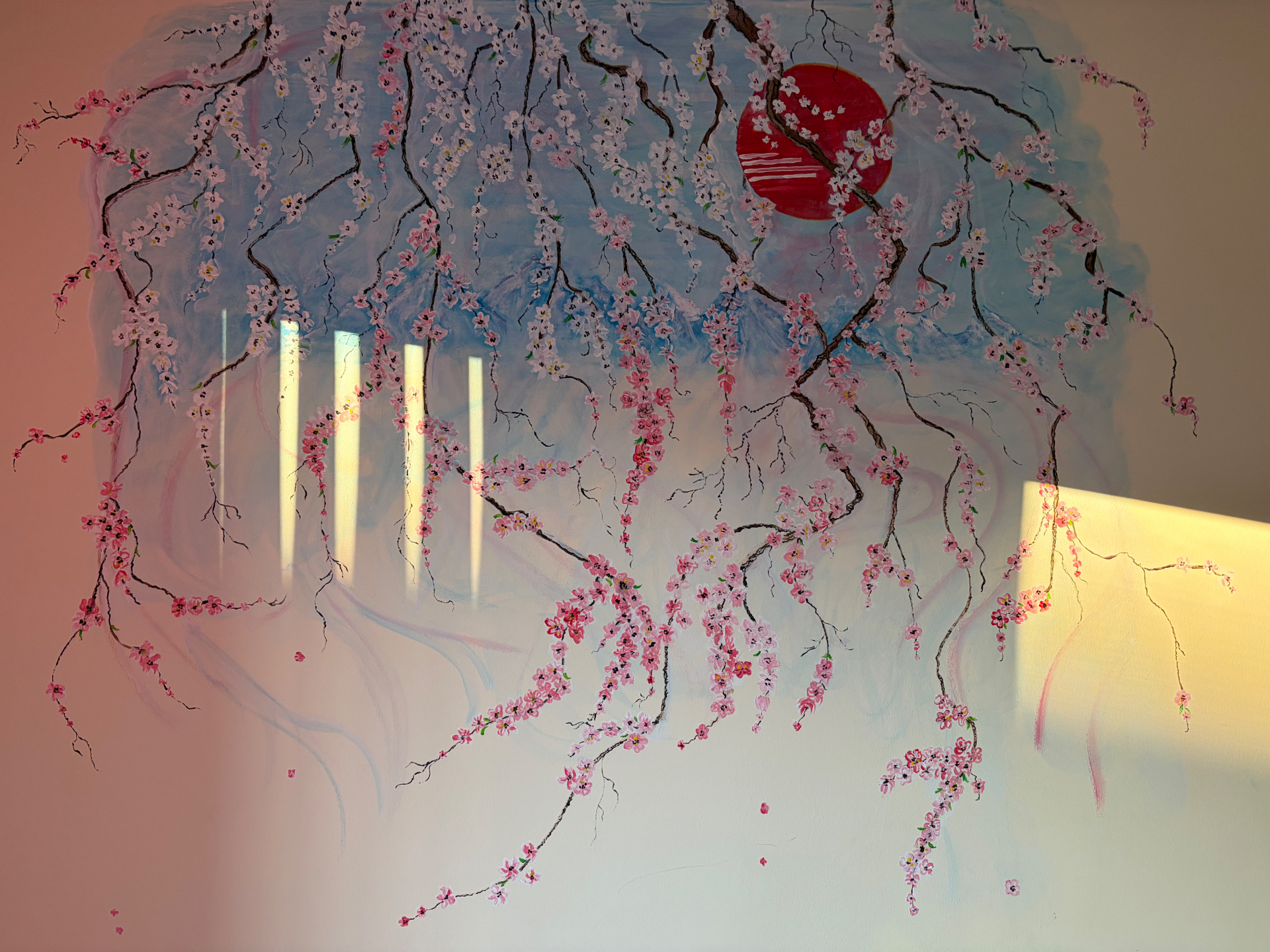 Full view of Nata Orlo’s Blossom Mural with flowering branches, blue mountains and a red sun